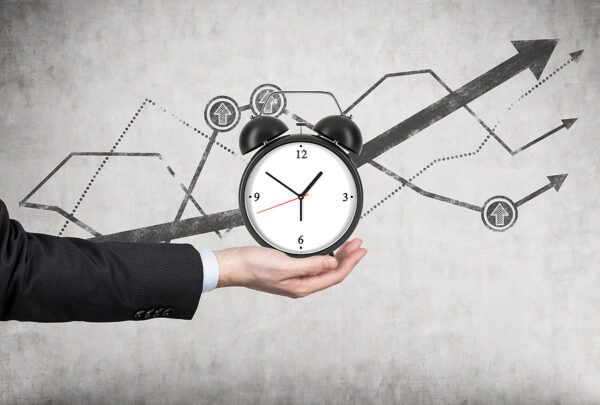A Businessman's Hand Holds An Alarm Clock. There Is A Growing Li