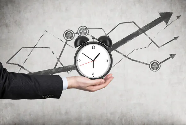 A Businessman's Hand Holds An Alarm Clock. There Is A Growing Li